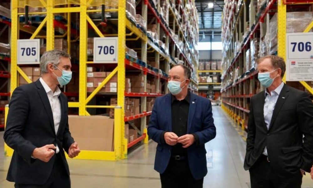 Le ministre Christian Dubé est entouré de deux hommes dans un entrepôt