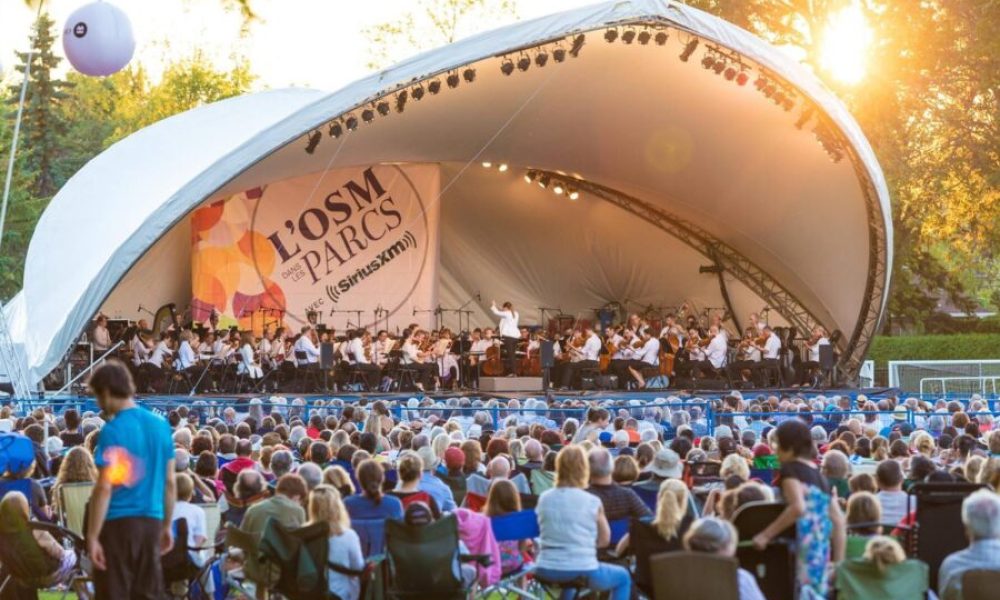 Des milliers de personnes assistent à un concert, les artistes sont sous un demi dôme en toile blanche.