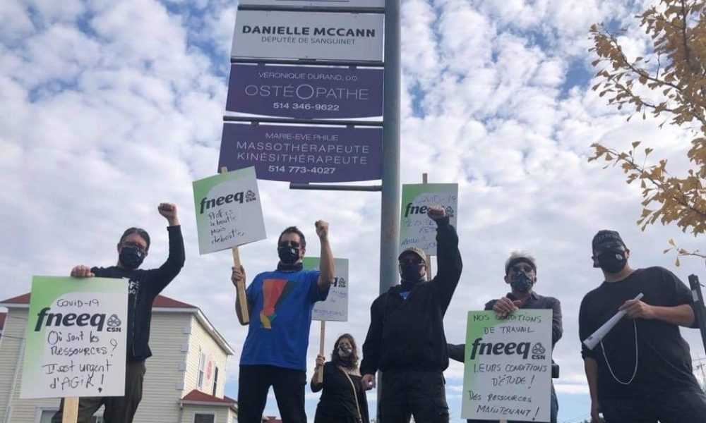 Des enseignants posent devant l'enseigne du bureau de la députée Danielle McCann pancartes à la main.
