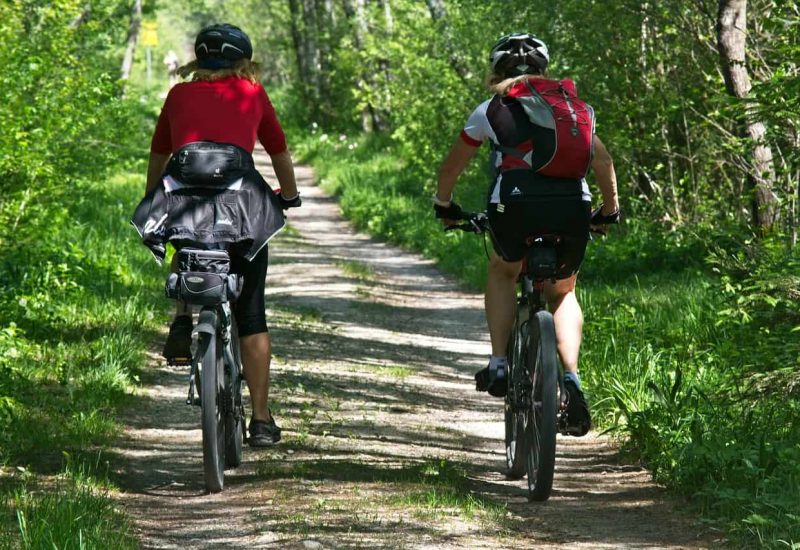 Deux cyclistes font du vélo sur une piste cyclable bordé d'arbres, ce qui inspirerait la trame verte de Beloeil.