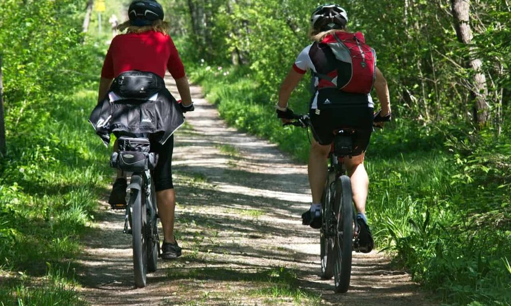 Deux cyclistes font du vélo sur une piste cyclable bordé d'arbres, ce qui inspirerait la trame verte de Beloeil.