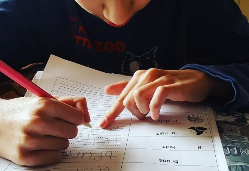 Un enfant, crayon à la main fait ses devoirs