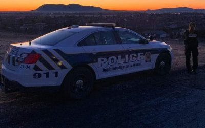 Une voiture de police du SPAL et une policère à ses côtés dans un coucher de soleil.