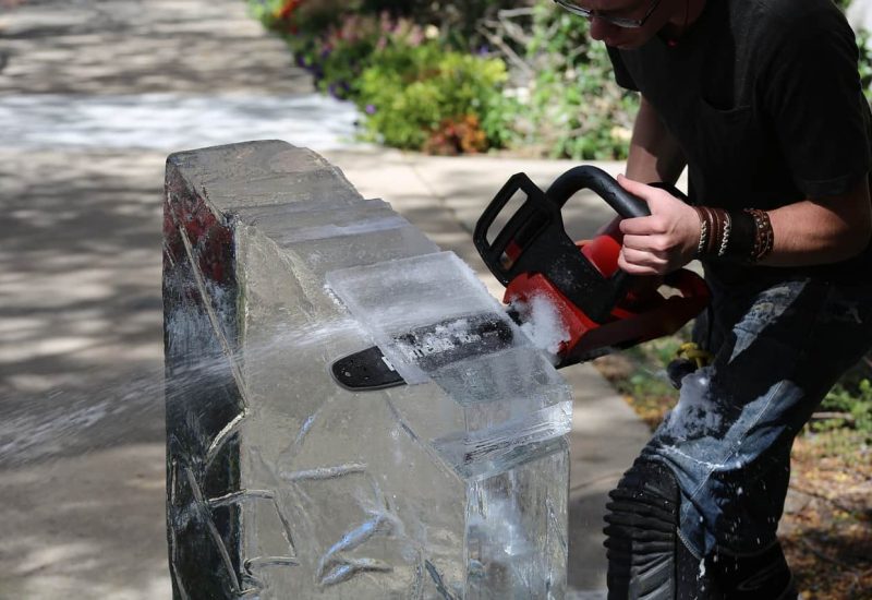 un homme sculpte un bloc de glace à la tronçonneuse
